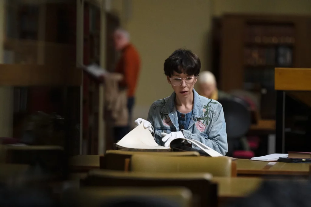 Langley (Sally Hawkins) est attablée dans une salle de lecture d'une bibliothèque. Elle tourne les pages d'un vieux et grand livre délicatement avec des gants blancs.